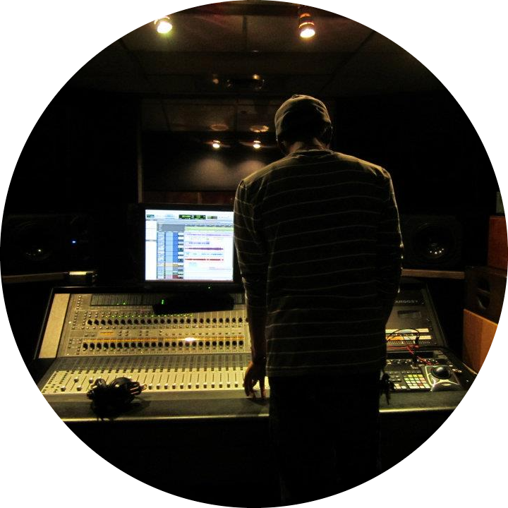 a music producer standing in front of a mixing board with Pro Tools on the computer screen